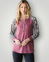 Woman wearing a pink long-sleeve top with patterned sleeves against a plain background
