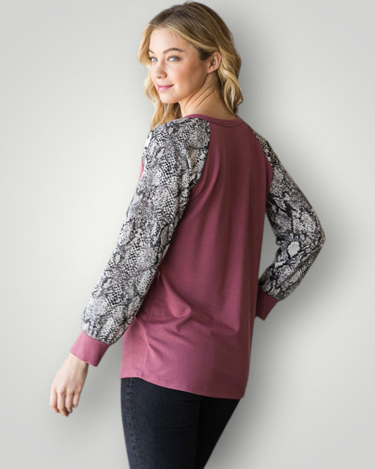 Woman wearing a maroon long-sleeve top with snake print sleeves against a white background