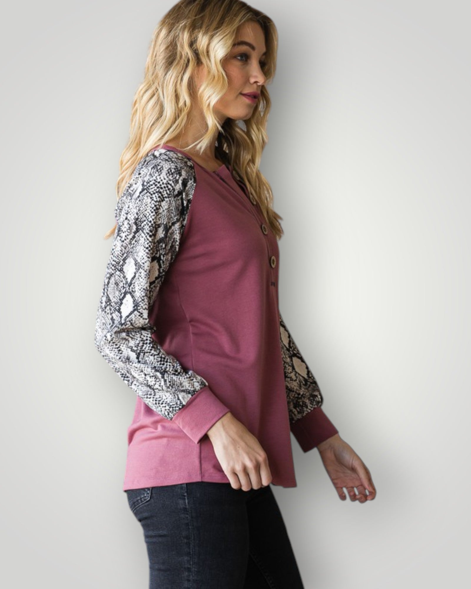 Woman wearing a pink top with snake print sleeves against a white background