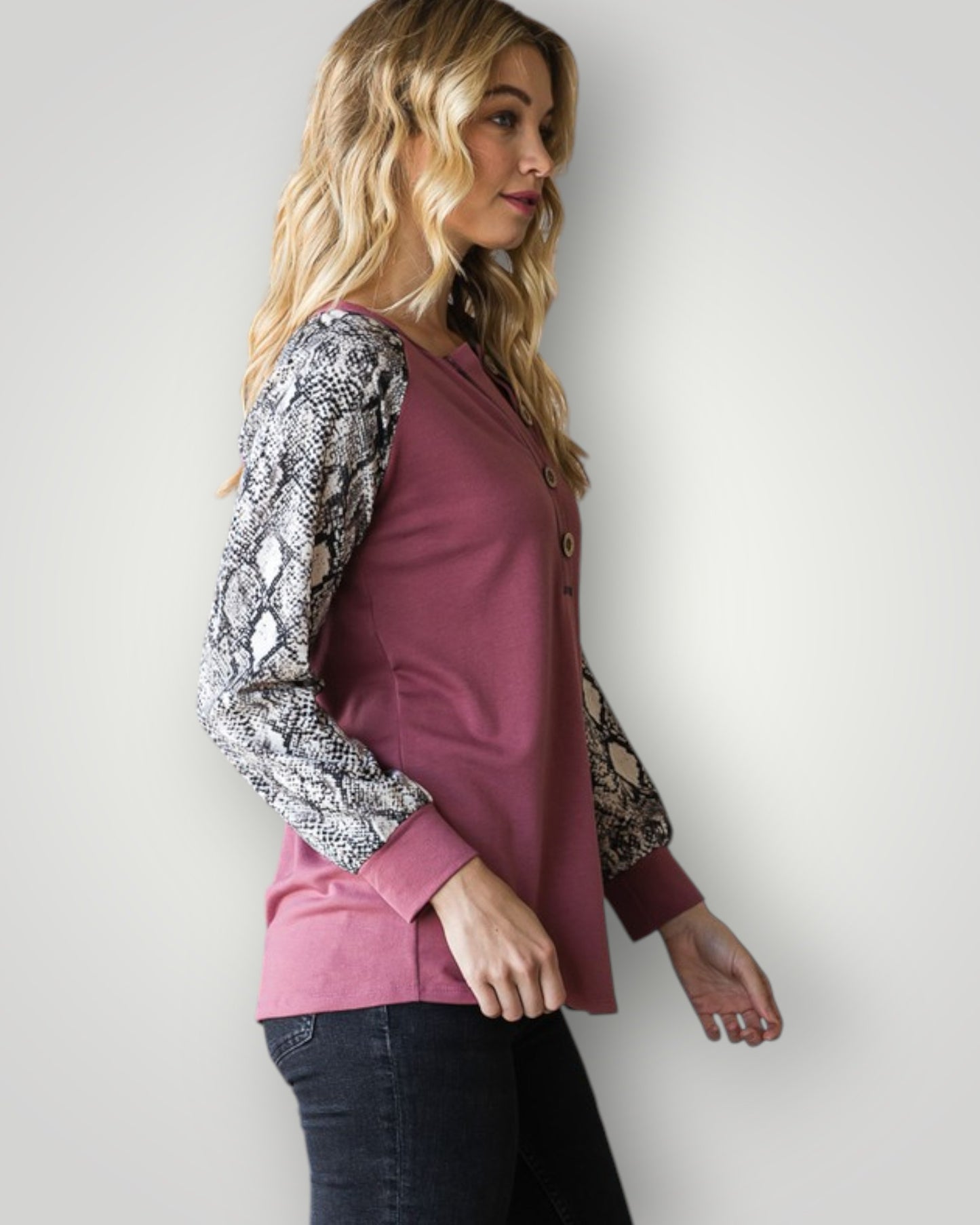 Woman wearing a pink top with snake print sleeves against a white background