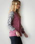Woman wearing a pink top with snake print sleeves against a white background