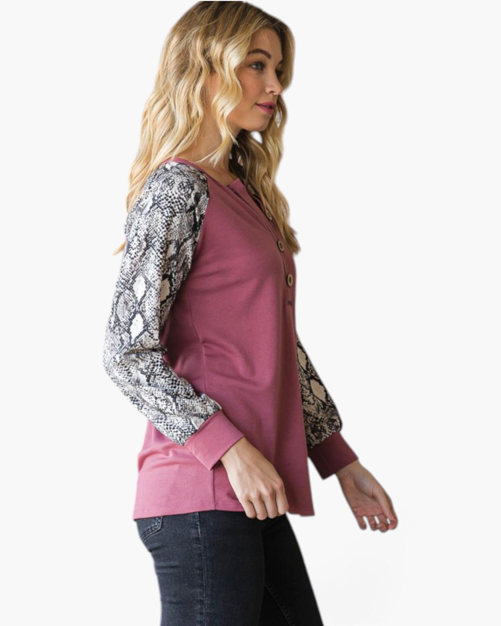 A woman wearing a dusty rose button-up top with snakeskin-patterned long sleeves, paired with dark jeans, shown from a side profile against a plain white background.