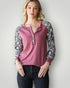 Woman wearing a pink long-sleeve top with snake print sleeves against a plain background