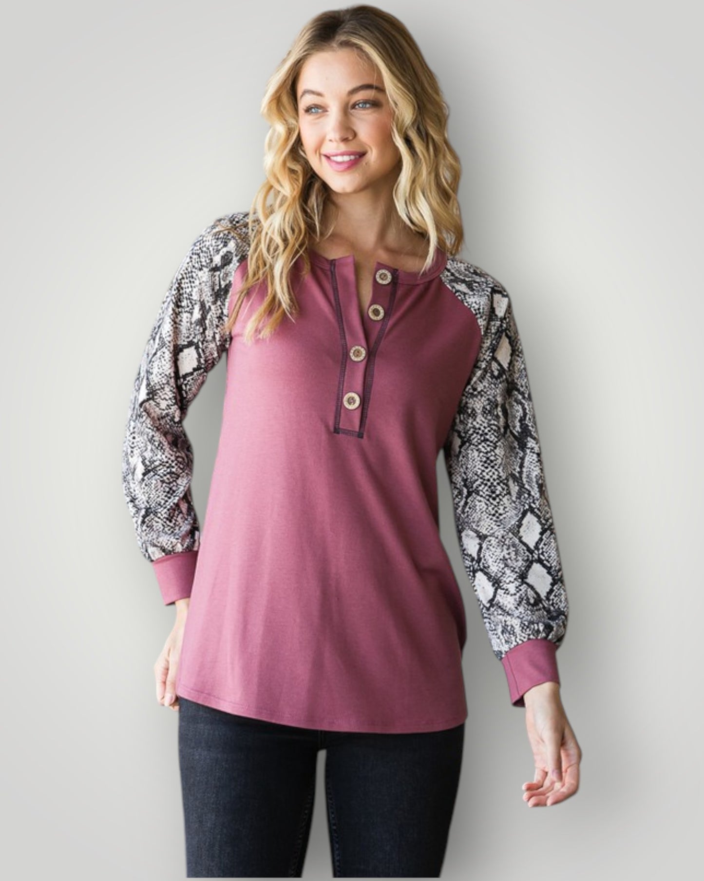 Woman wearing a pink long-sleeve top with snake print sleeves against a plain background