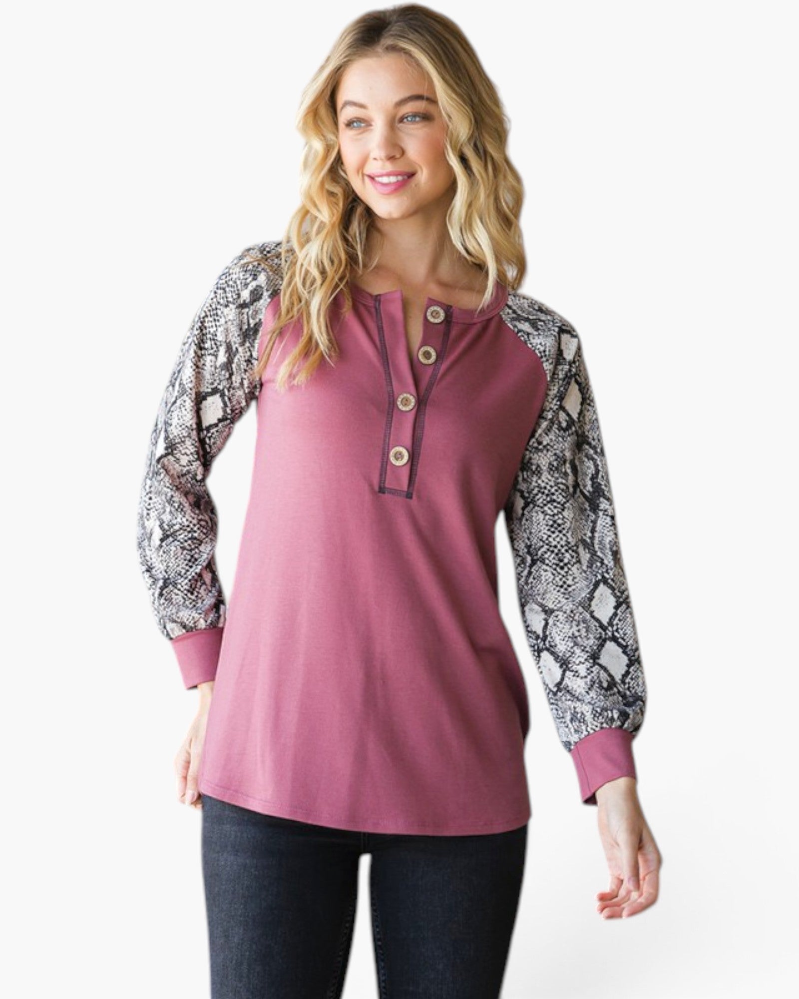 A woman modeling a long-sleeve henley top with a solid dusty rose body and snakeskin-patterned sleeves, paired with dark jeans against a plain white background.