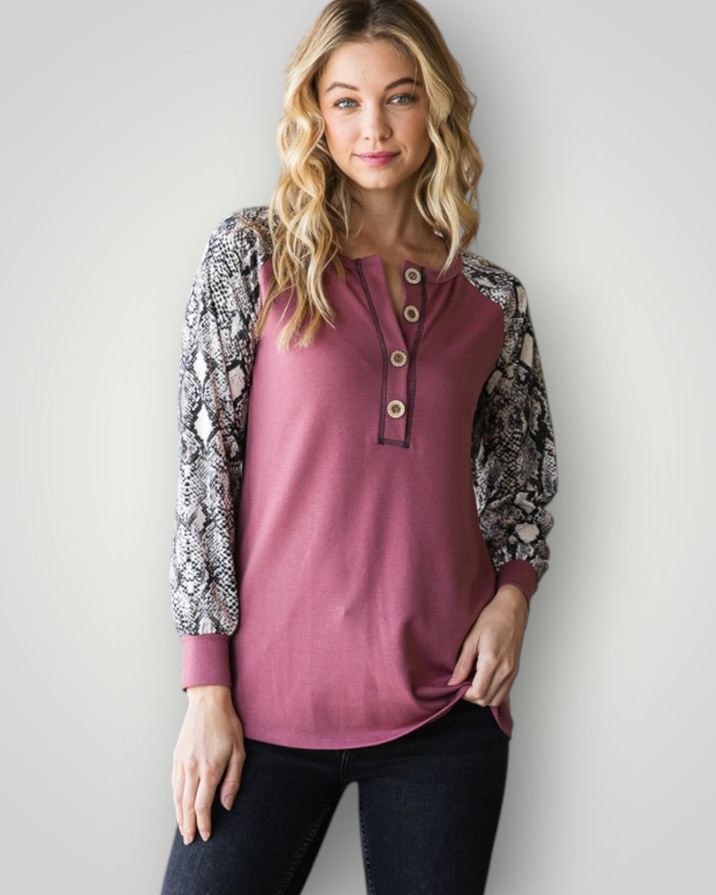 Woman wearing a pink long-sleeve top with patterned sleeves against a plain background