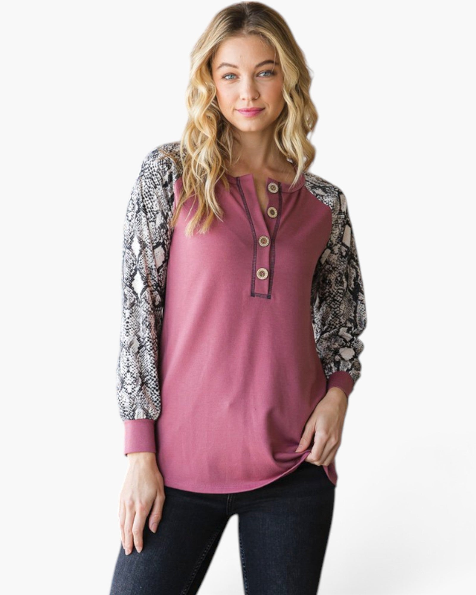 A woman modeling a long-sleeve henley top with a solid dusty rose body and snakeskin-patterned sleeves, paired with dark jeans against a plain white background.