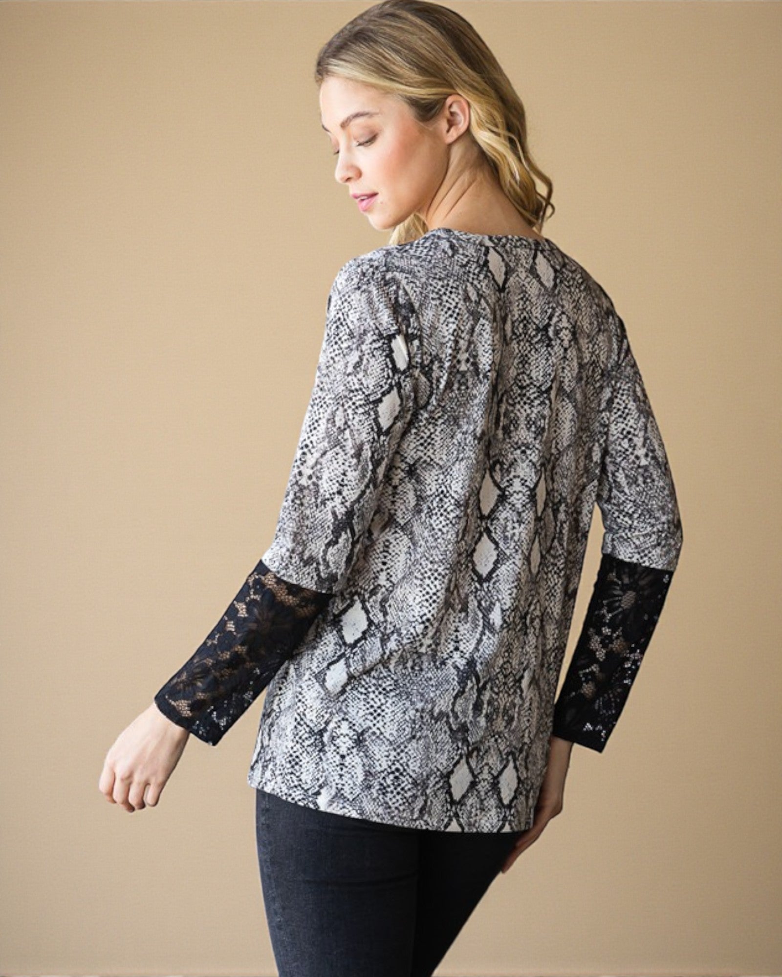 Woman wearing a snake print top with lace sleeves on a beige background