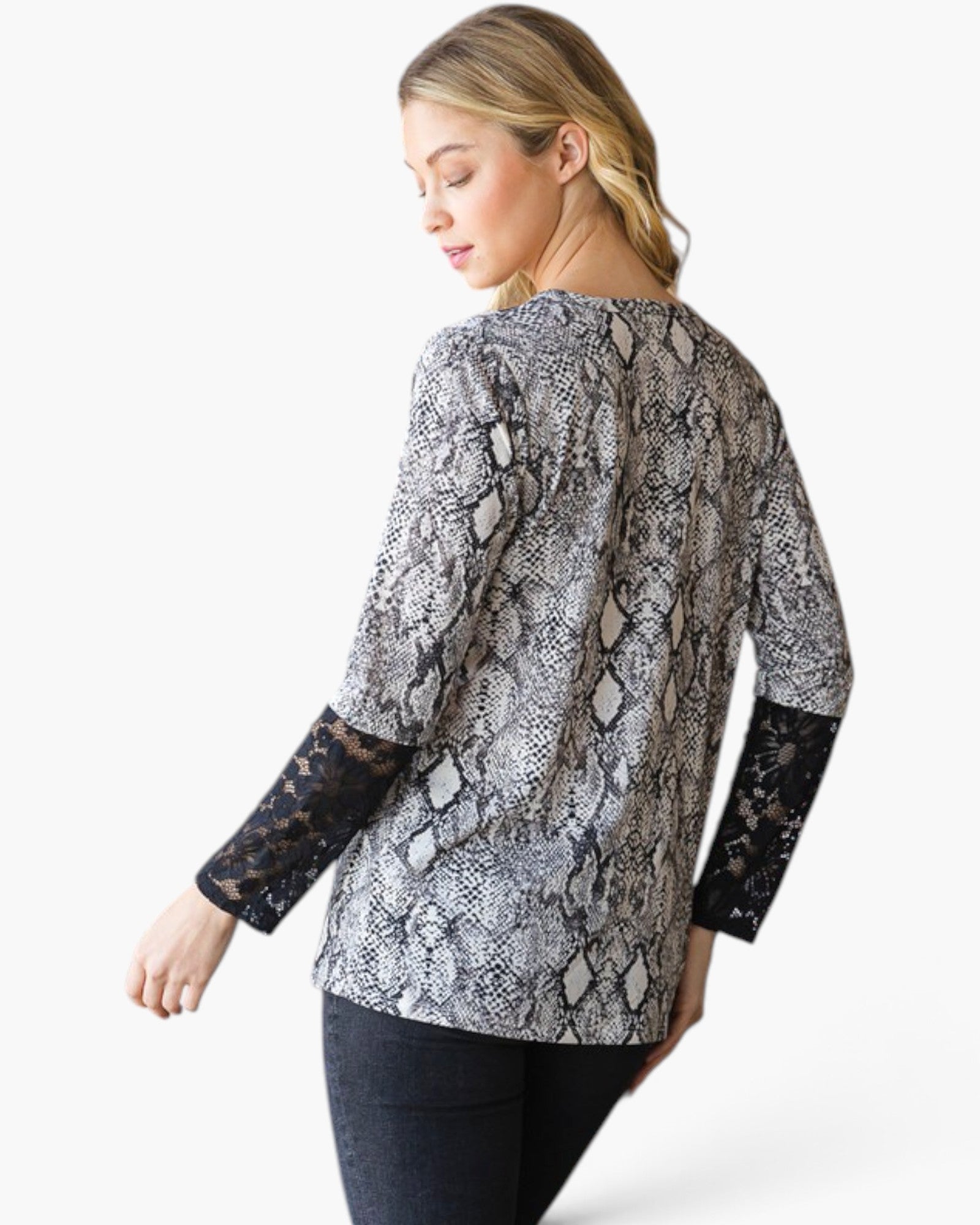 A woman shown from the back wearing a long-sleeve top with a gray and black snakeskin pattern and black lace cuffs, paired with dark jeans, against a plain white studio background.