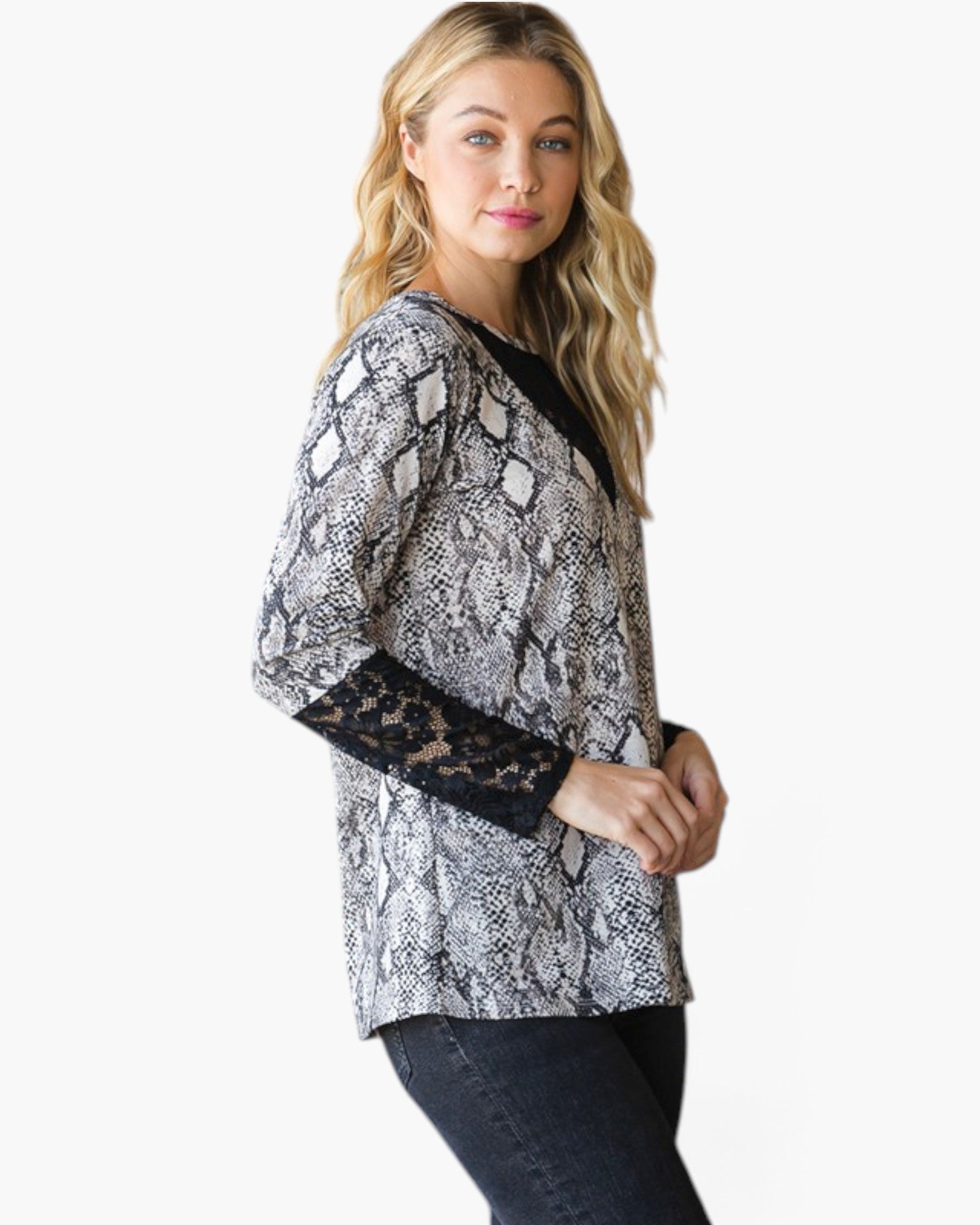A woman modeling a long-sleeve top with a black and white snakeskin pattern and black lace cuffs, paired with dark jeans, against a plain white background.