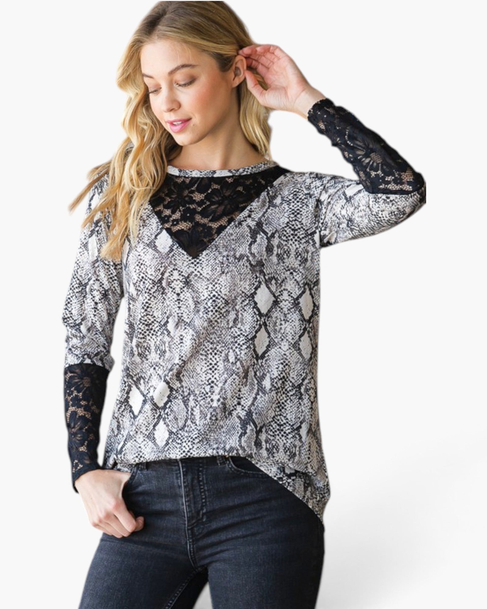 A woman modeling a long-sleeve top with a gray and black snakeskin pattern, black lace V-neckline, and black lace cuffs, paired with dark blue jeans against a white studio background.