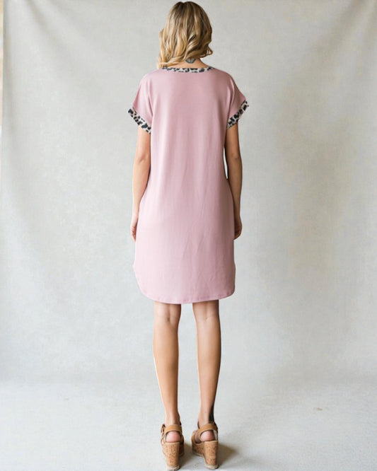 Woman wearing a pink dress with leopard print accents on a plain background