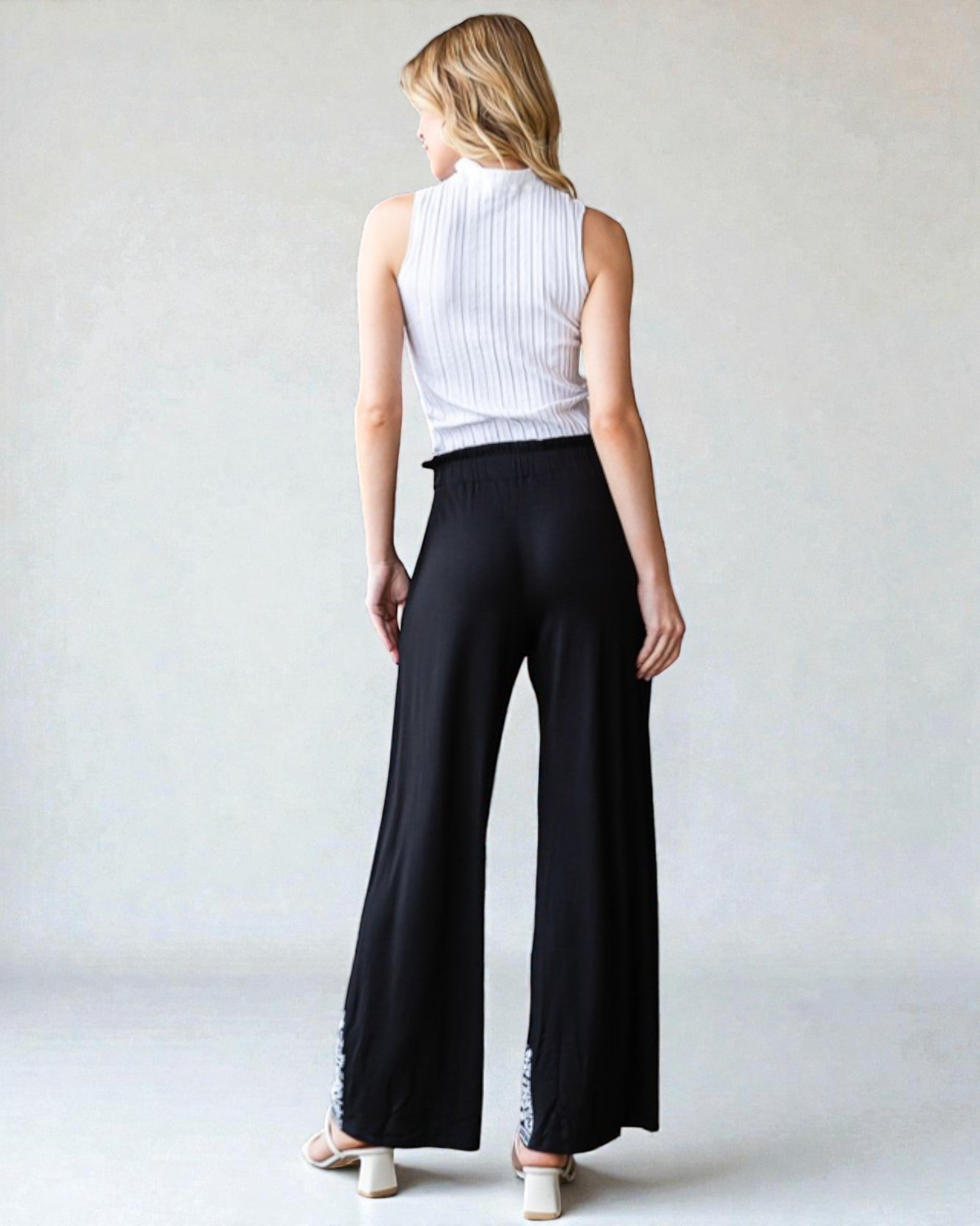 Woman wearing a white sleeveless top and black wide-leg pants on a plain background