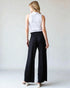 Woman wearing a white sleeveless top and black wide-leg pants on a plain background