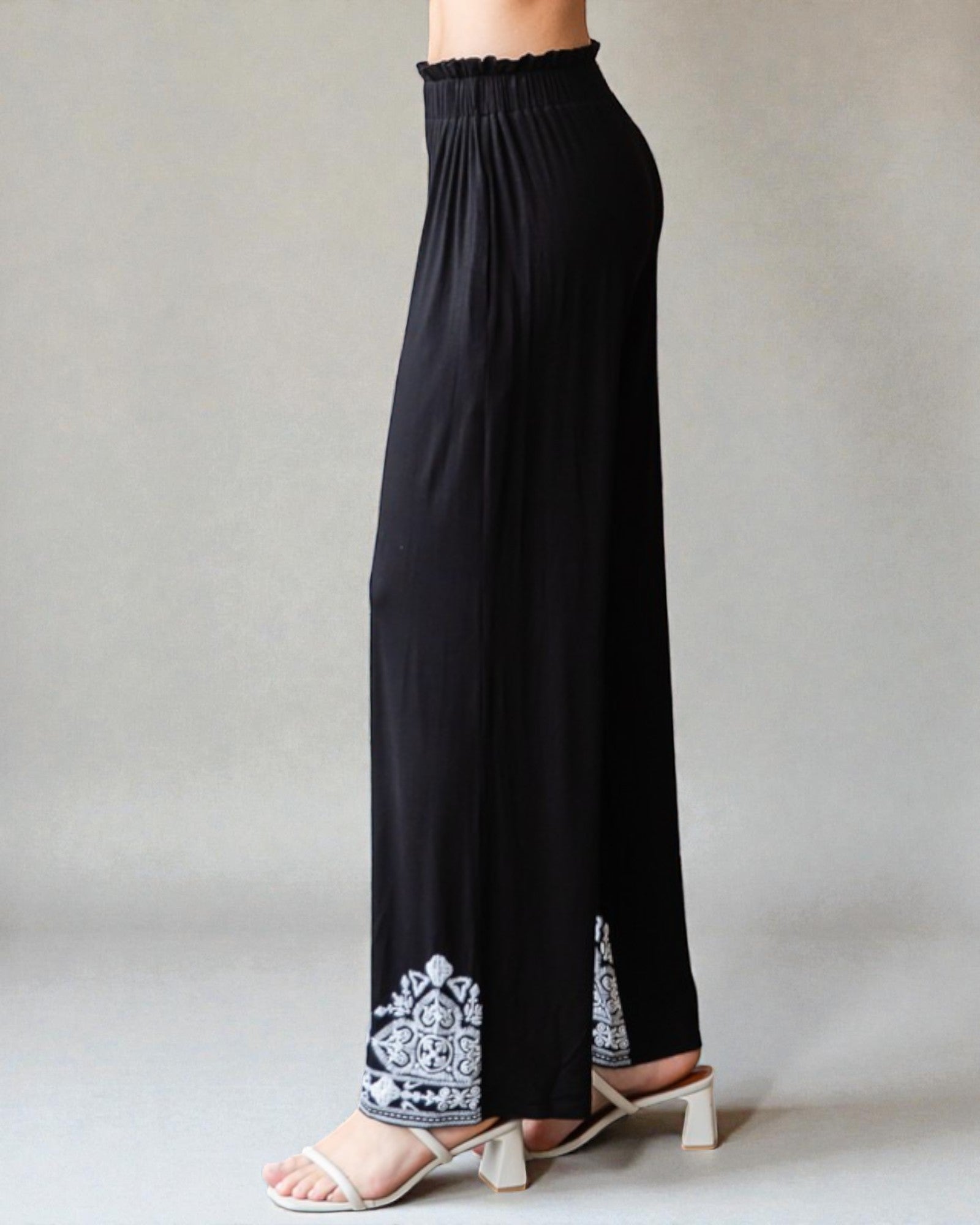 Black pants with white embroidery on a neutral background