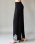 Black pants with white embroidery on a neutral background