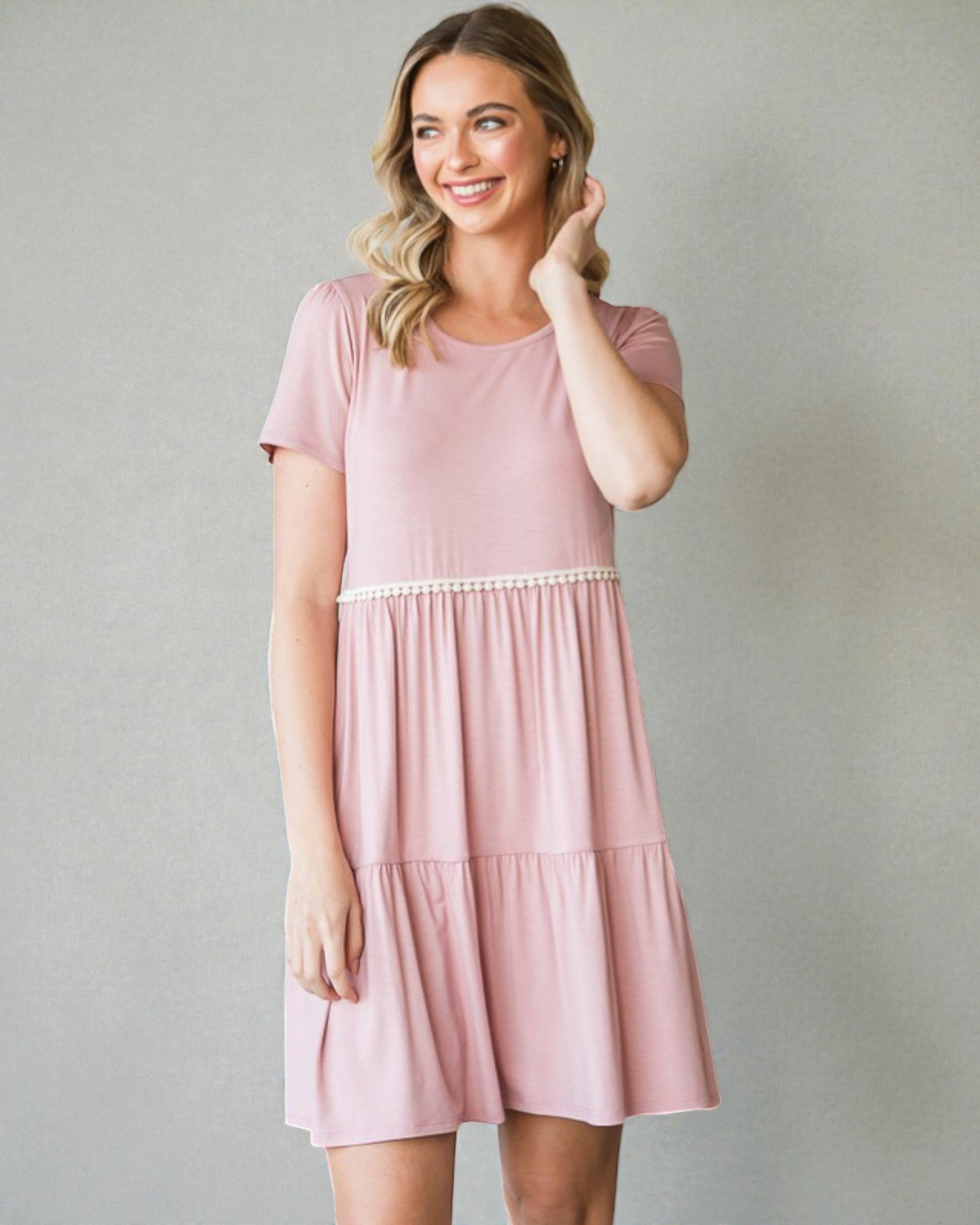 Woman wearing a pink dress with a white waistband against a gray background