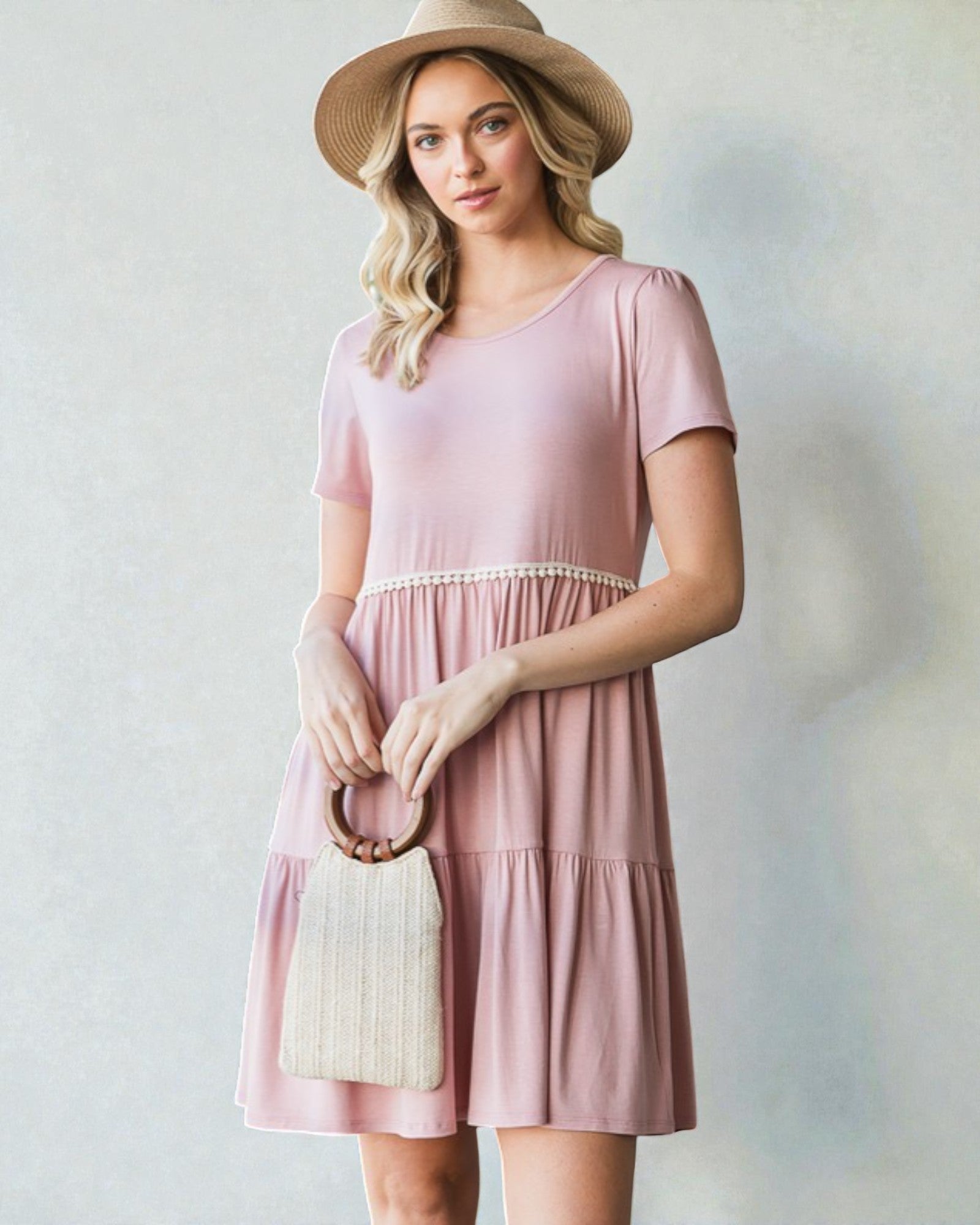 Woman wearing a pink dress and straw hat against a neutral background
