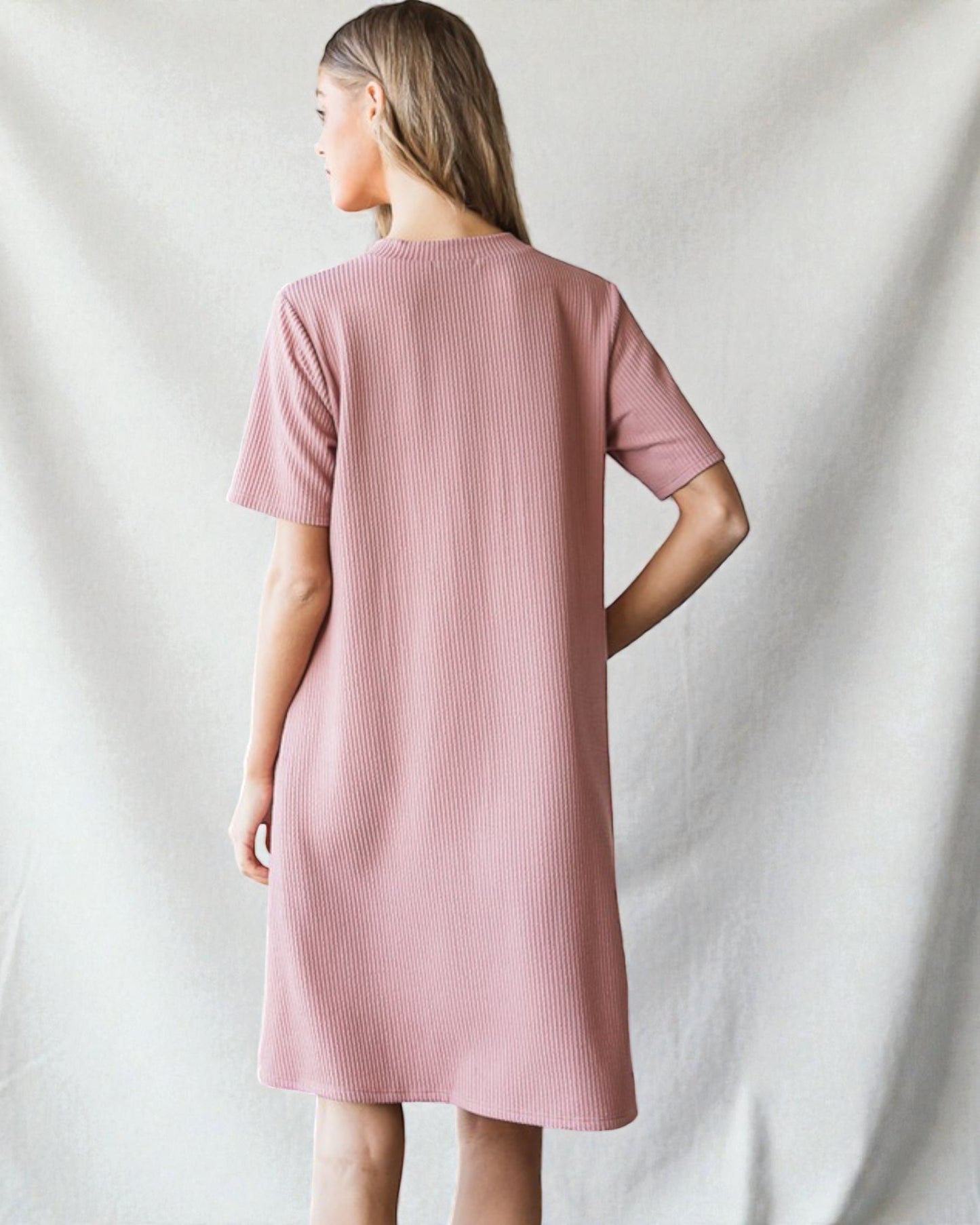 Woman wearing a pink ribbed dress against a plain background