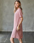 Woman wearing a pink dress against a gray wall.