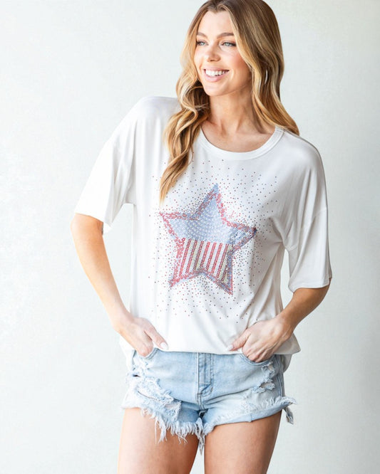 Woman wearing a white t-shirt with a star graphic and denim shorts on a plain background