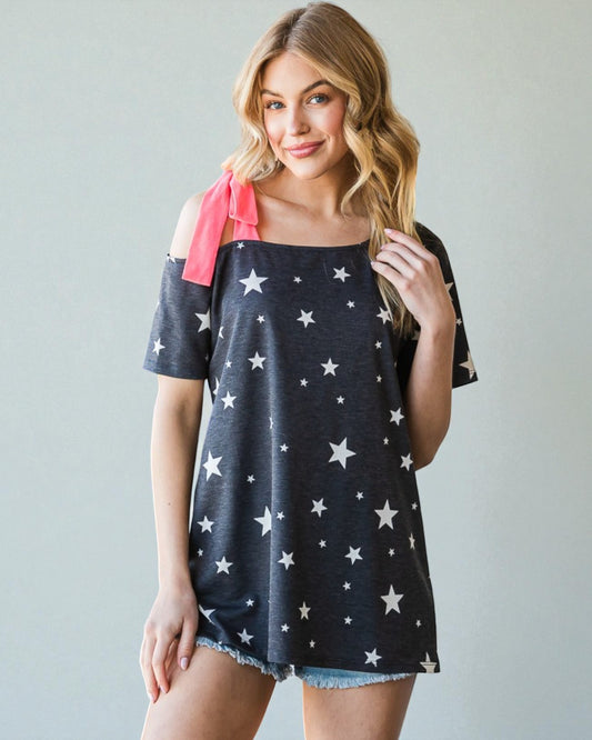 Woman wearing a navy blue top with white star patterns and denim shorts on a plain background