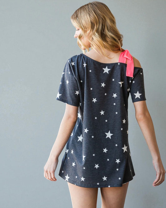 Woman wearing a navy dress with white star patterns and a pink bow on a gray background