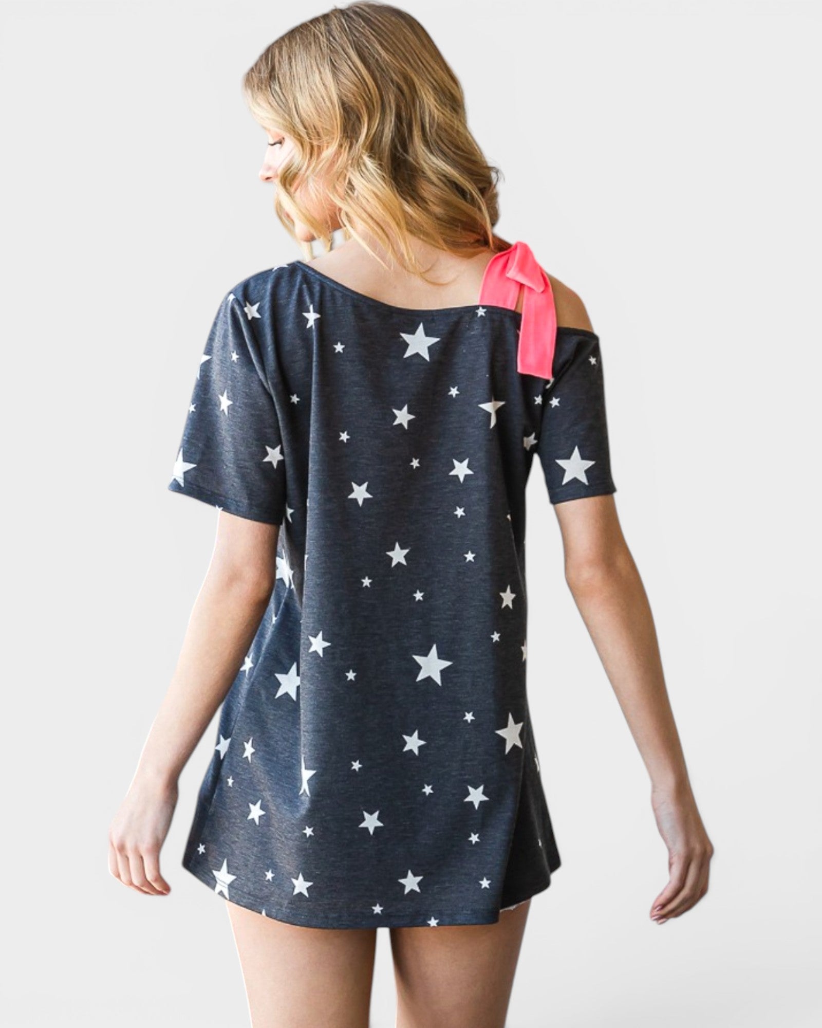 Woman wearing a navy blue dress with white star patterns and a pink ribbon on a plain background