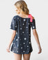 Woman wearing a navy blue dress with white star patterns and a pink ribbon on a plain background