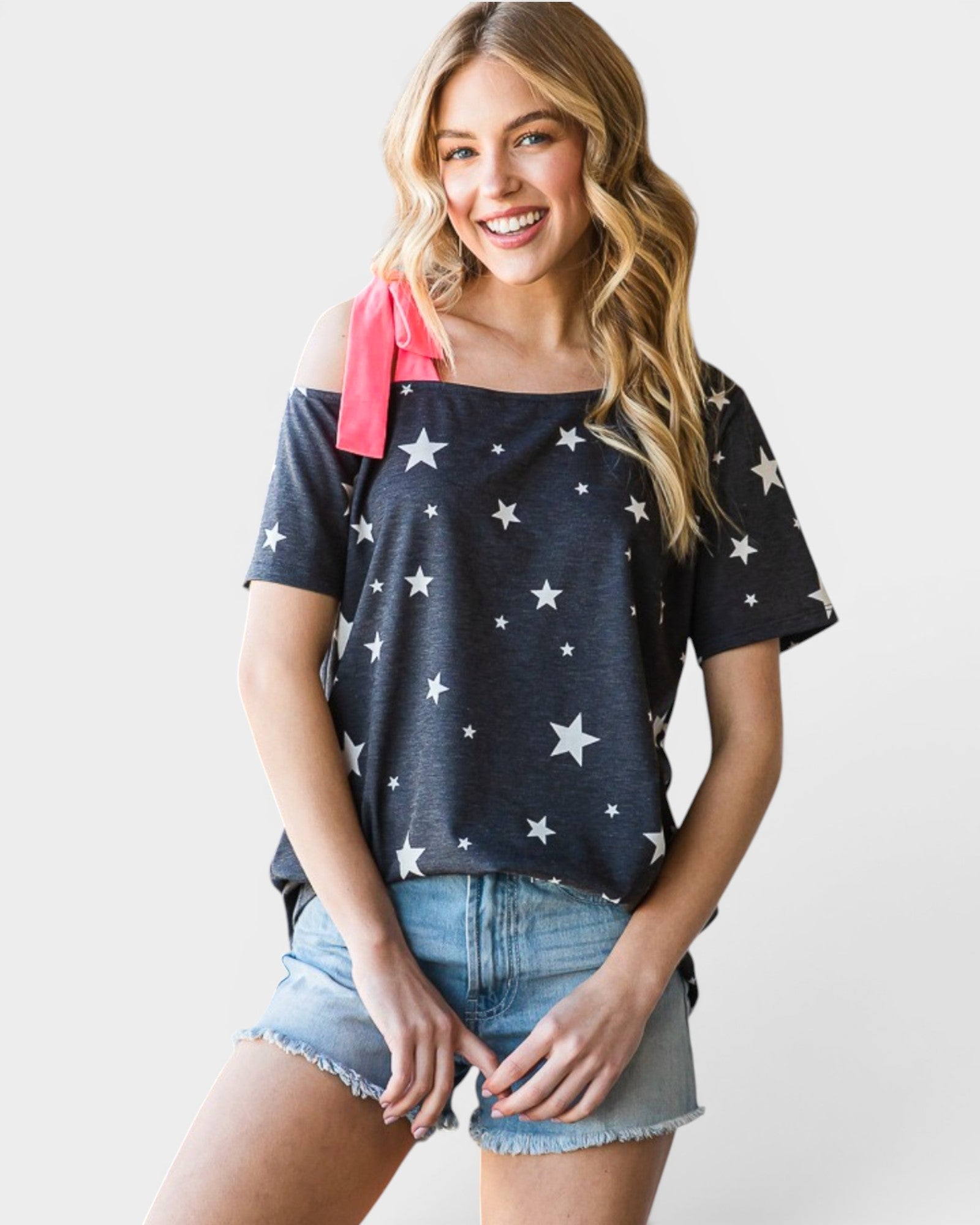 Woman wearing a navy blue off-shoulder top with white star patterns and denim shorts on a plain background