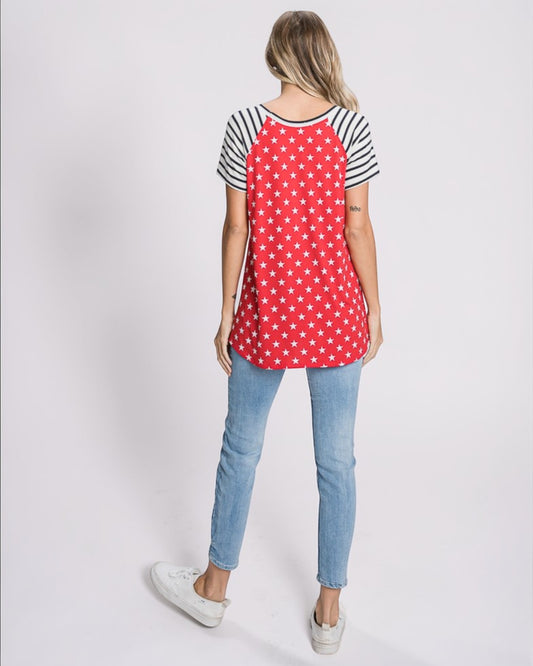 Woman wearing a red polka dot shirt with black and white sleeves and blue jeans on a light gray background