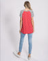 Woman wearing a red polka dot shirt with black and white sleeves and blue jeans on a light gray background
