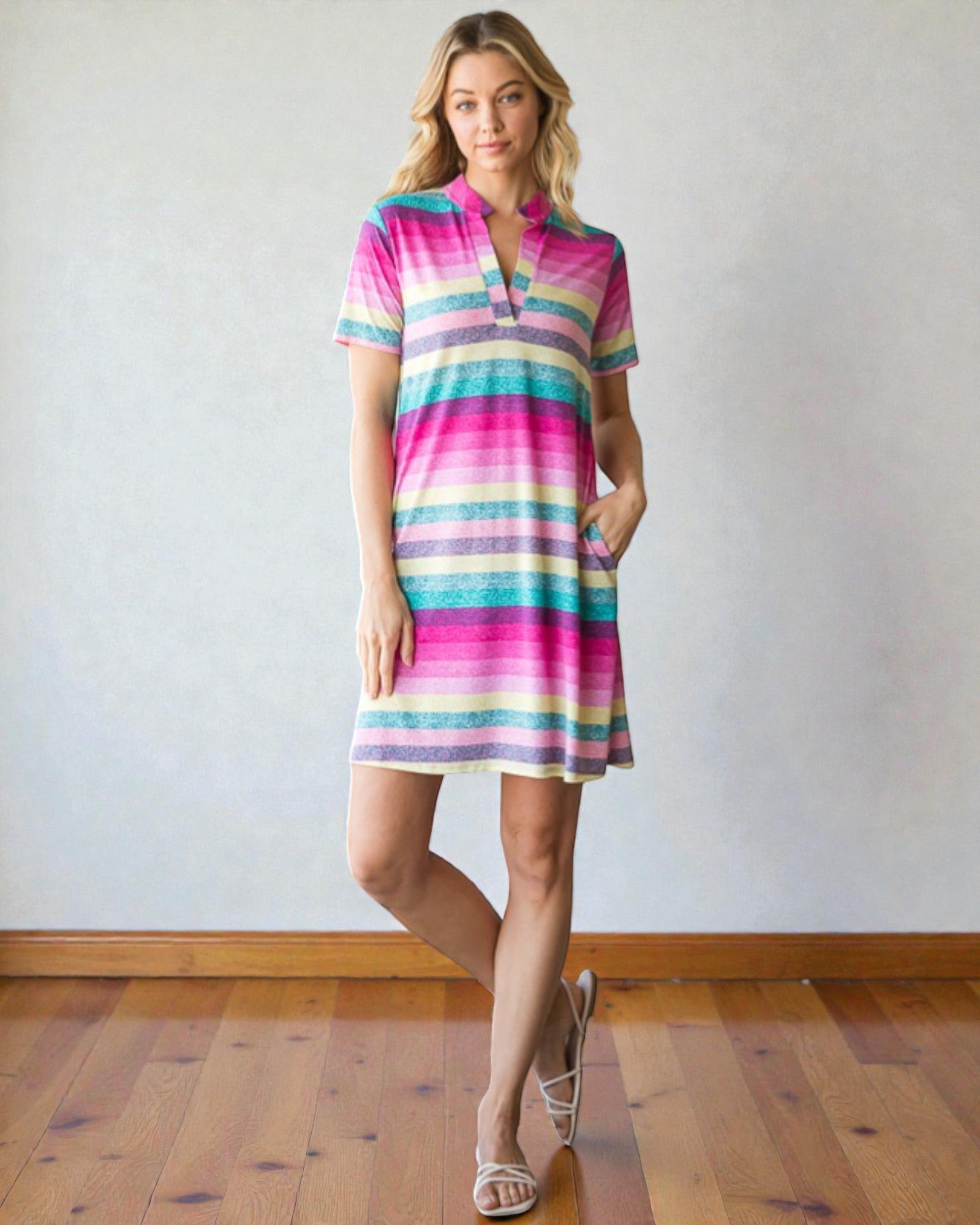 Woman wearing a colorful striped dress standing against a plain wall.