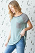 Woman wearing a light blue t-shirt with a pocket design against a textured white wall.