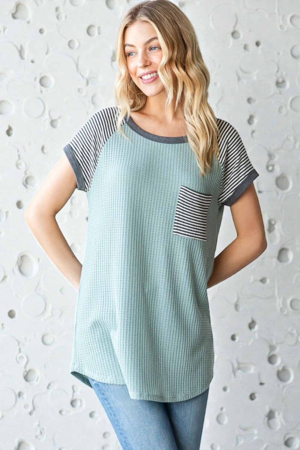 Woman wearing a green and gray patterned top against a textured white background