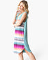 A woman modeling a sleeveless, high-low dress with a solid teal blue back panel and a side panel featuring horizontal stripes in pink, orange, yellow, green, blue, and purple, against a plain white background.