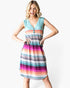 A woman modeling a sleeveless V-neck dress with horizontal stripes in shades of teal, orange, pink, purple, gray, and white, set against a plain light gray background.