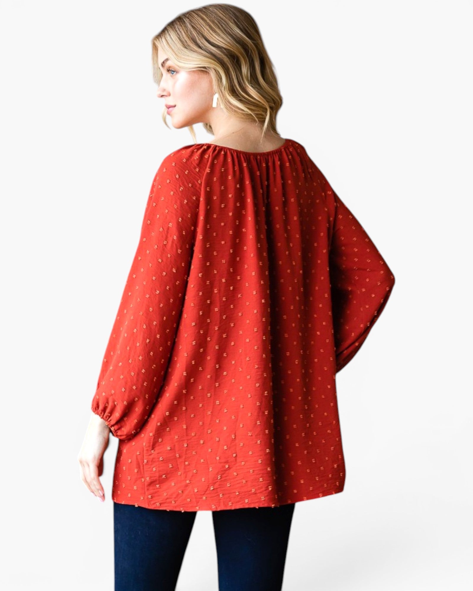 A woman shown from the back wearing a loose red top with a small white polka dot pattern and dark blue jeans, photographed against a light gray studio background.