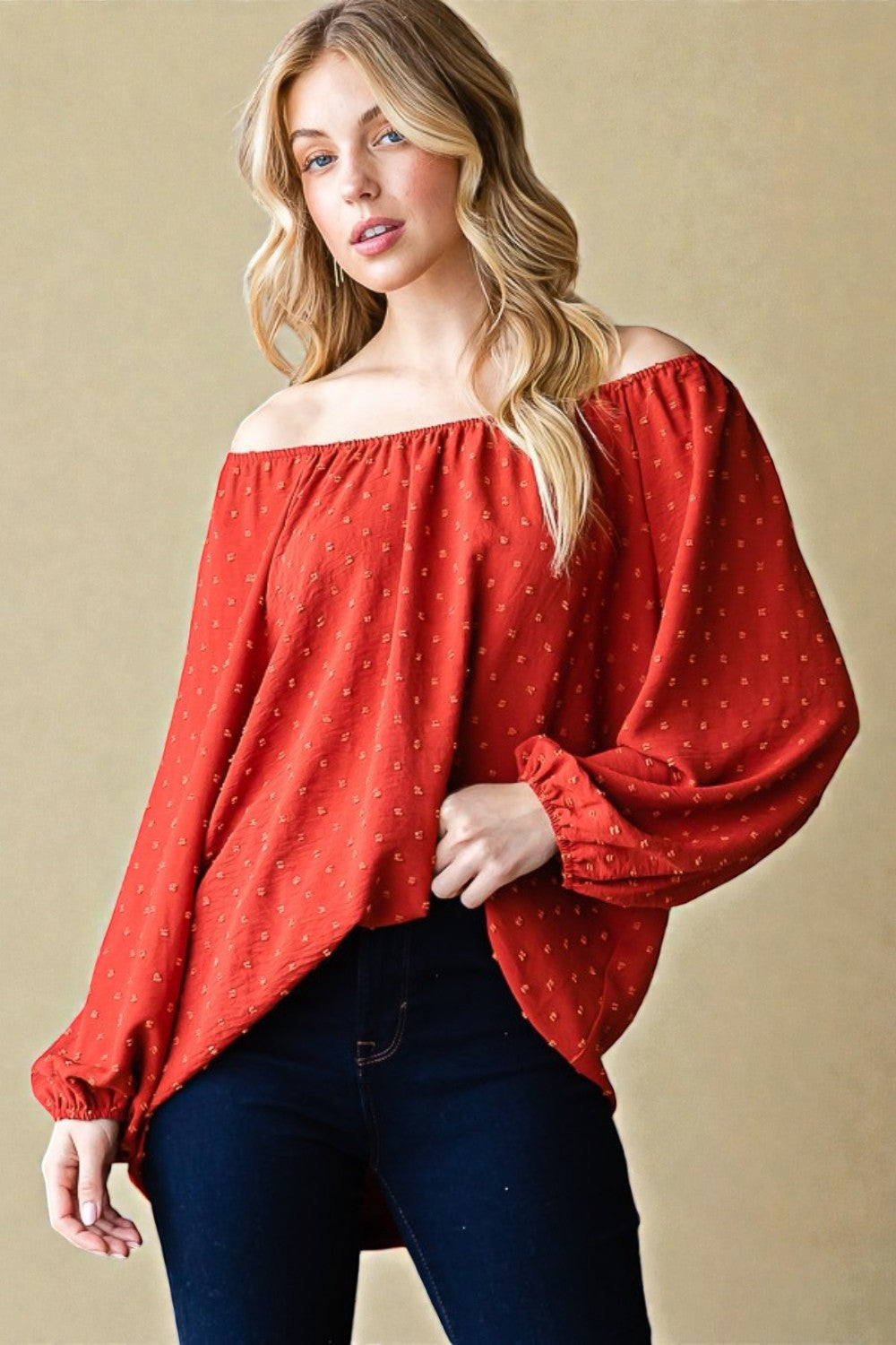 Woman wearing a red off-shoulder blouse with long sleeves against a beige background