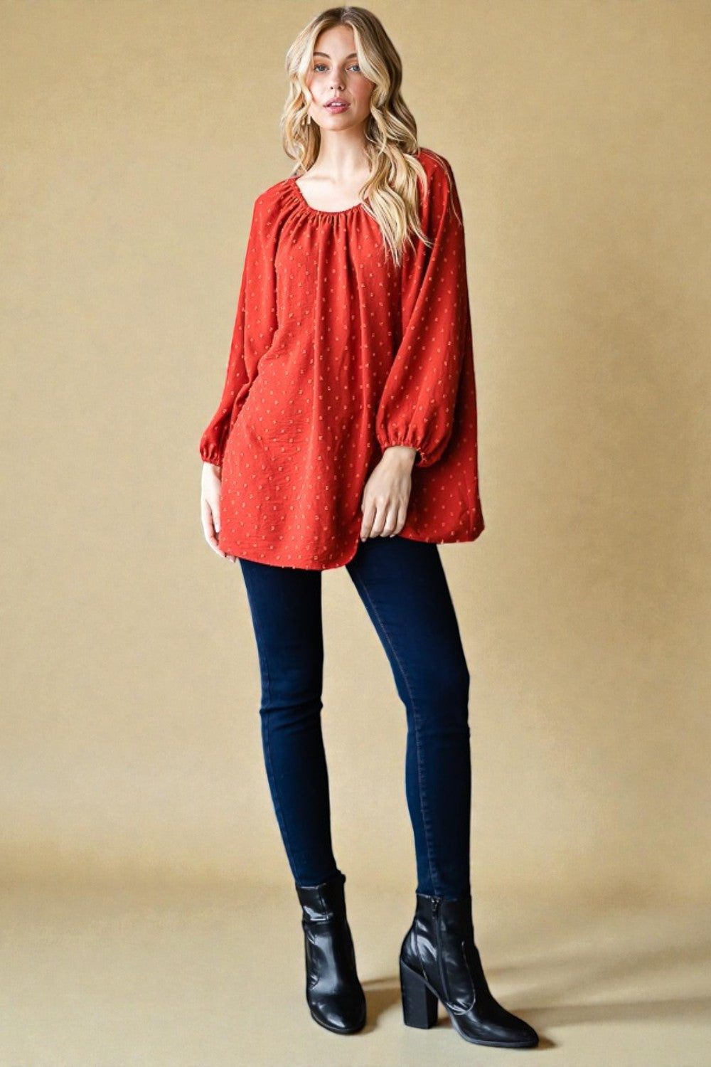Woman wearing a red sweater, dark jeans, and black boots against a beige background