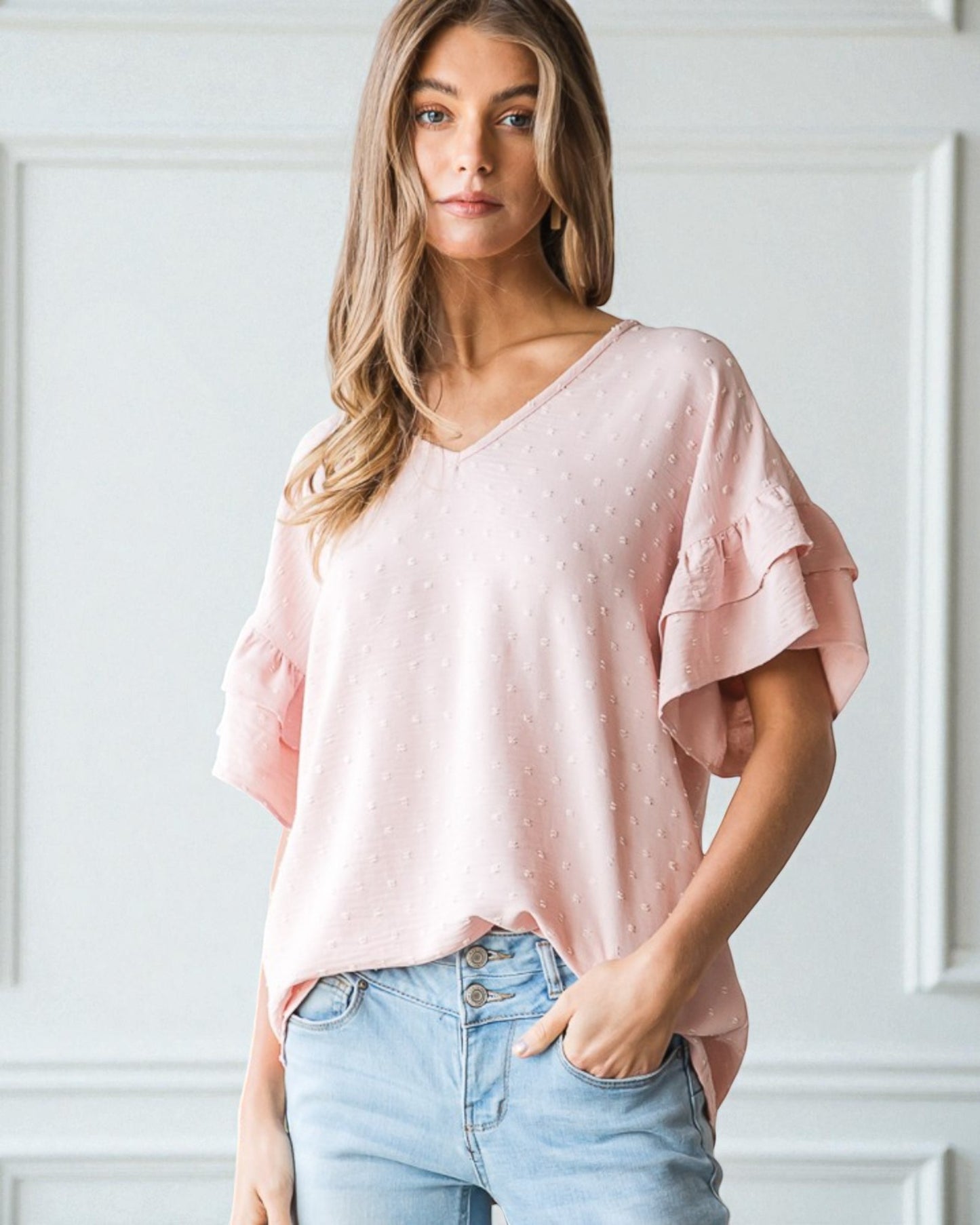 Woman wearing a pink blouse with ruffled sleeves against a white wall