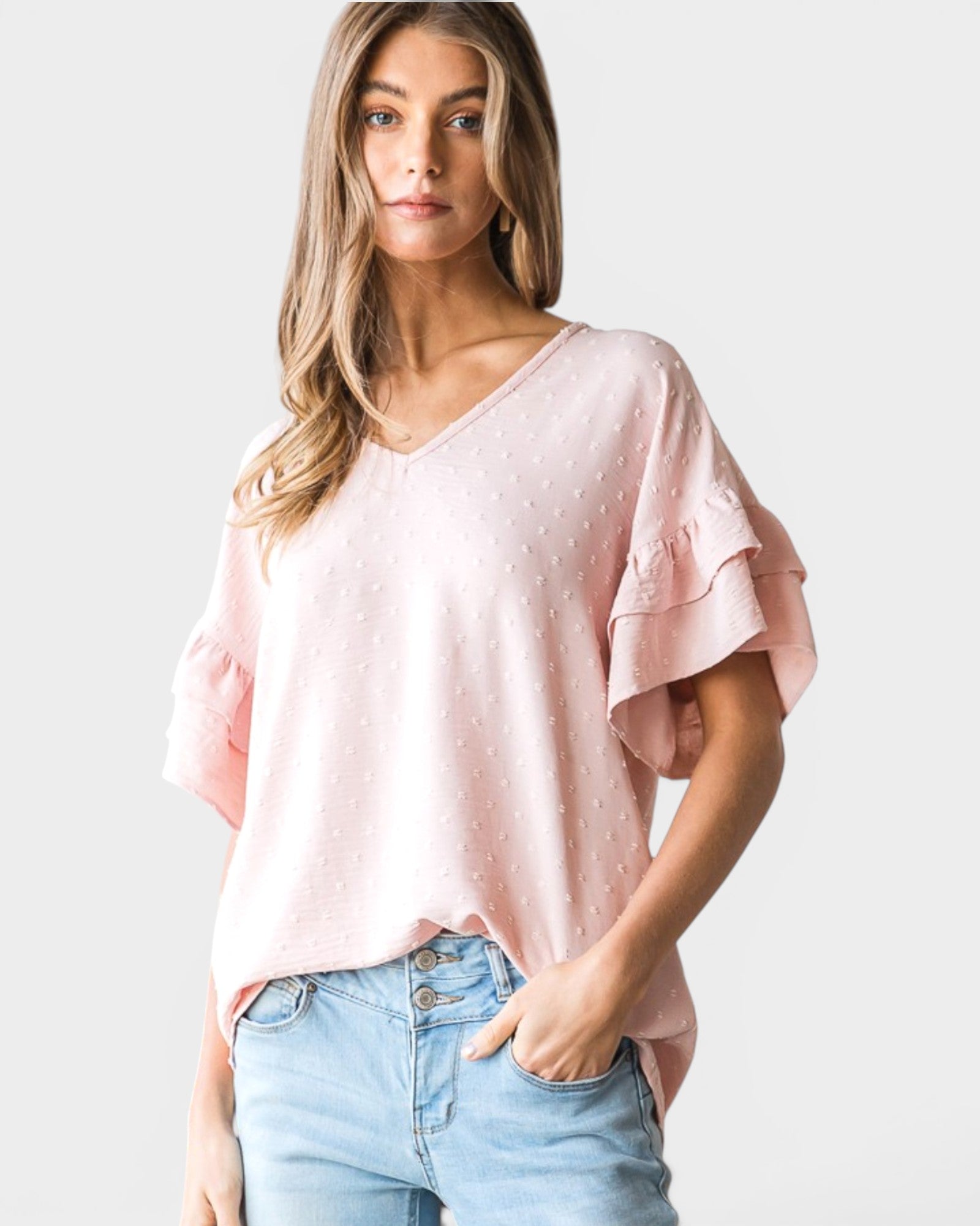 Woman wearing a pink blouse with ruffled sleeves and light blue jeans on a white background