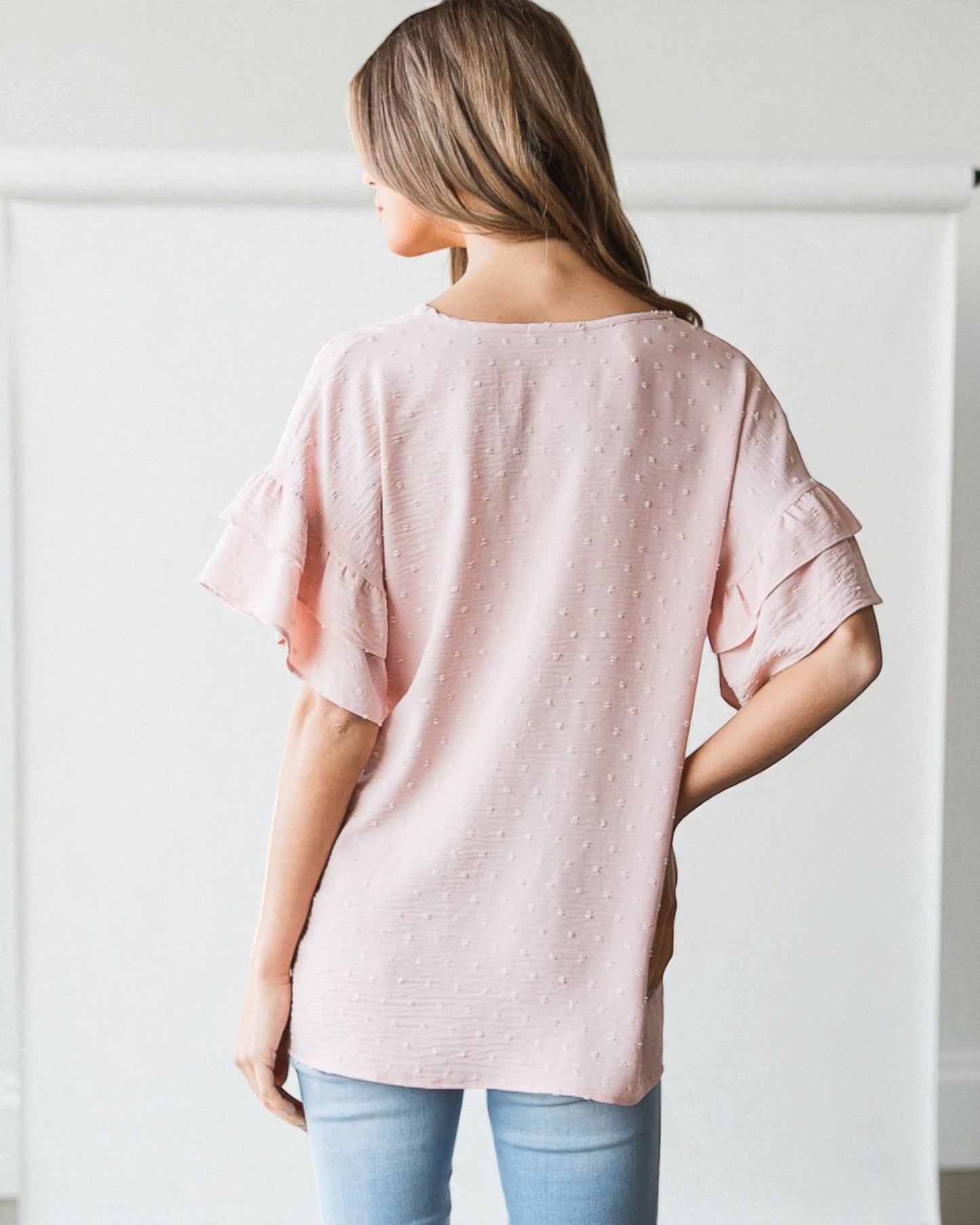 Woman wearing a pink blouse with ruffled sleeves against a white background