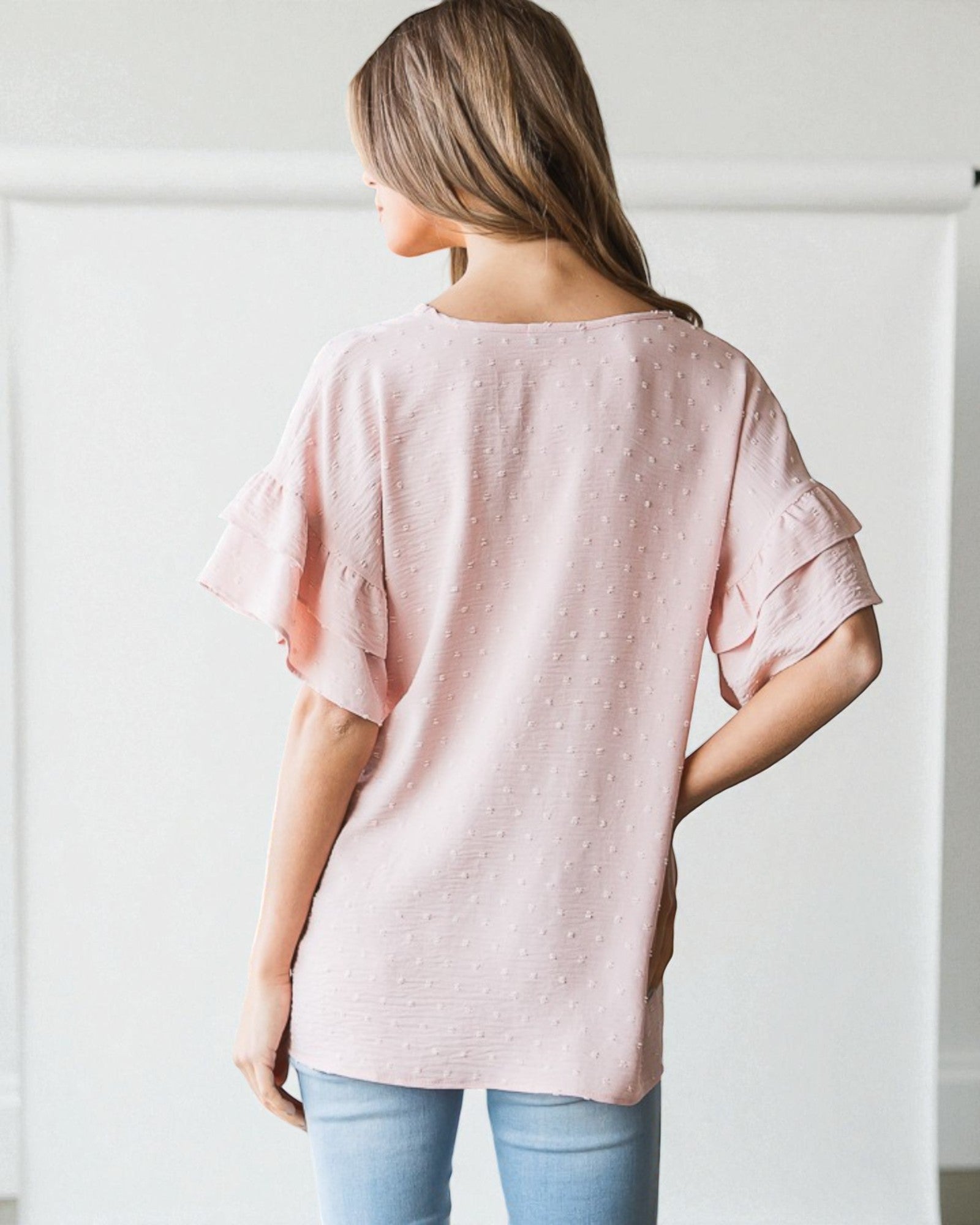 Woman wearing a pink blouse with ruffled sleeves against a white background