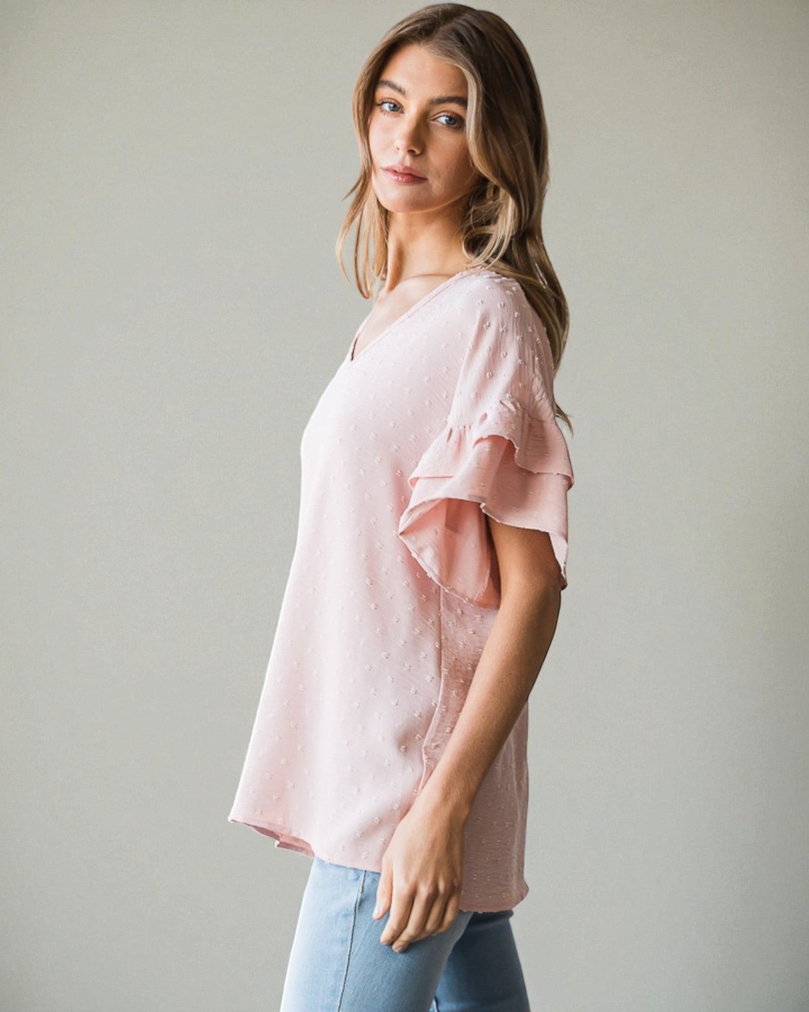 Woman wearing a pink blouse with ruffled sleeves against a plain background