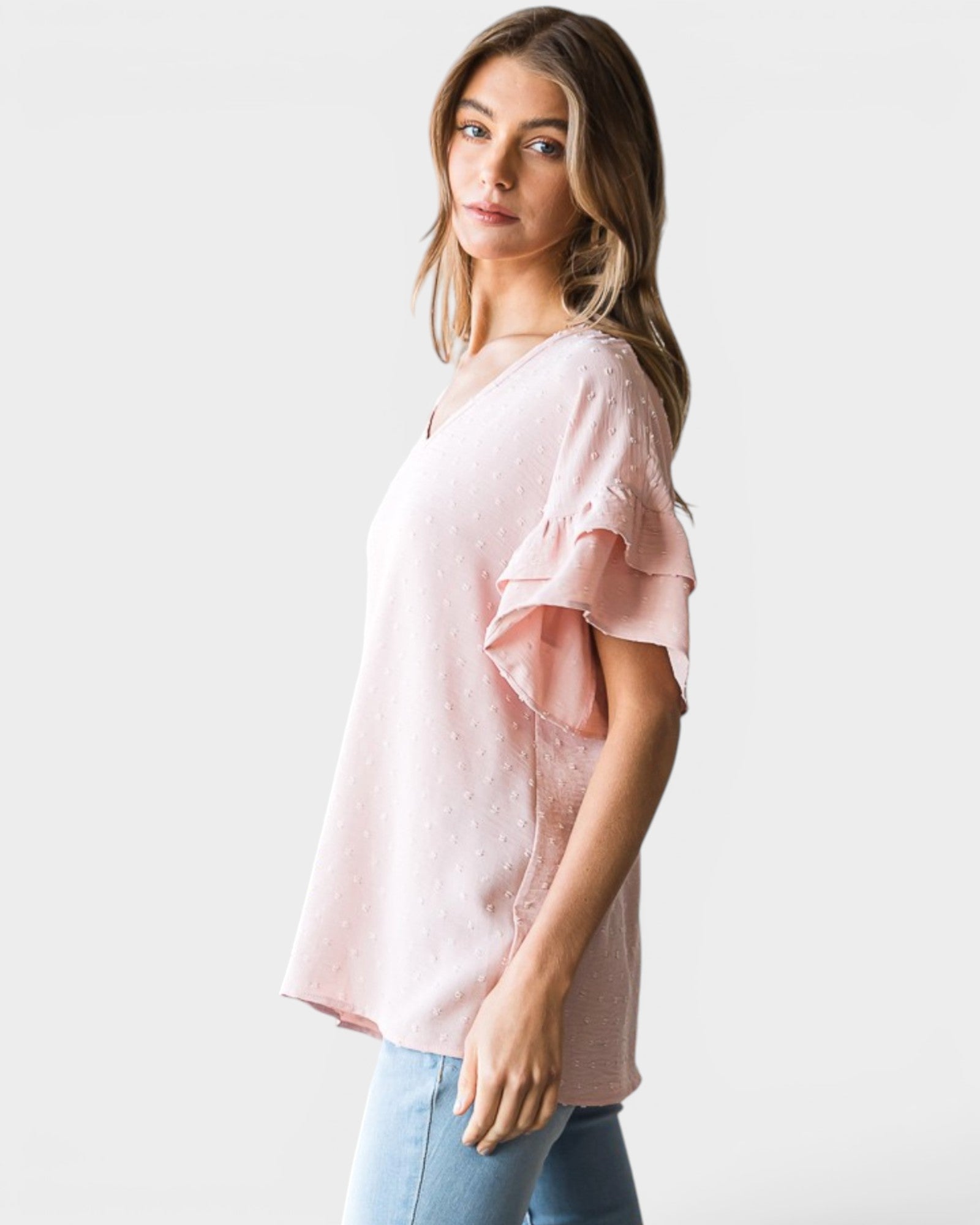 Woman wearing a light pink blouse with ruffled sleeves on a plain background