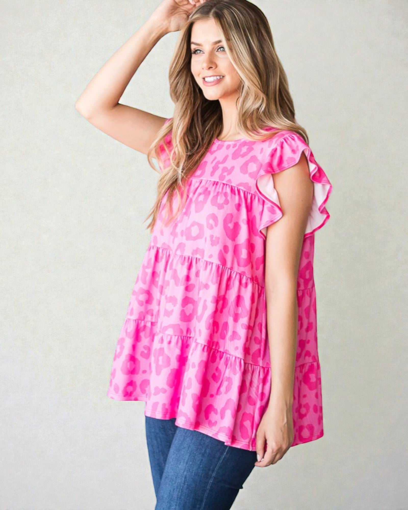 Woman wearing a pink patterned top with blue jeans on a plain background