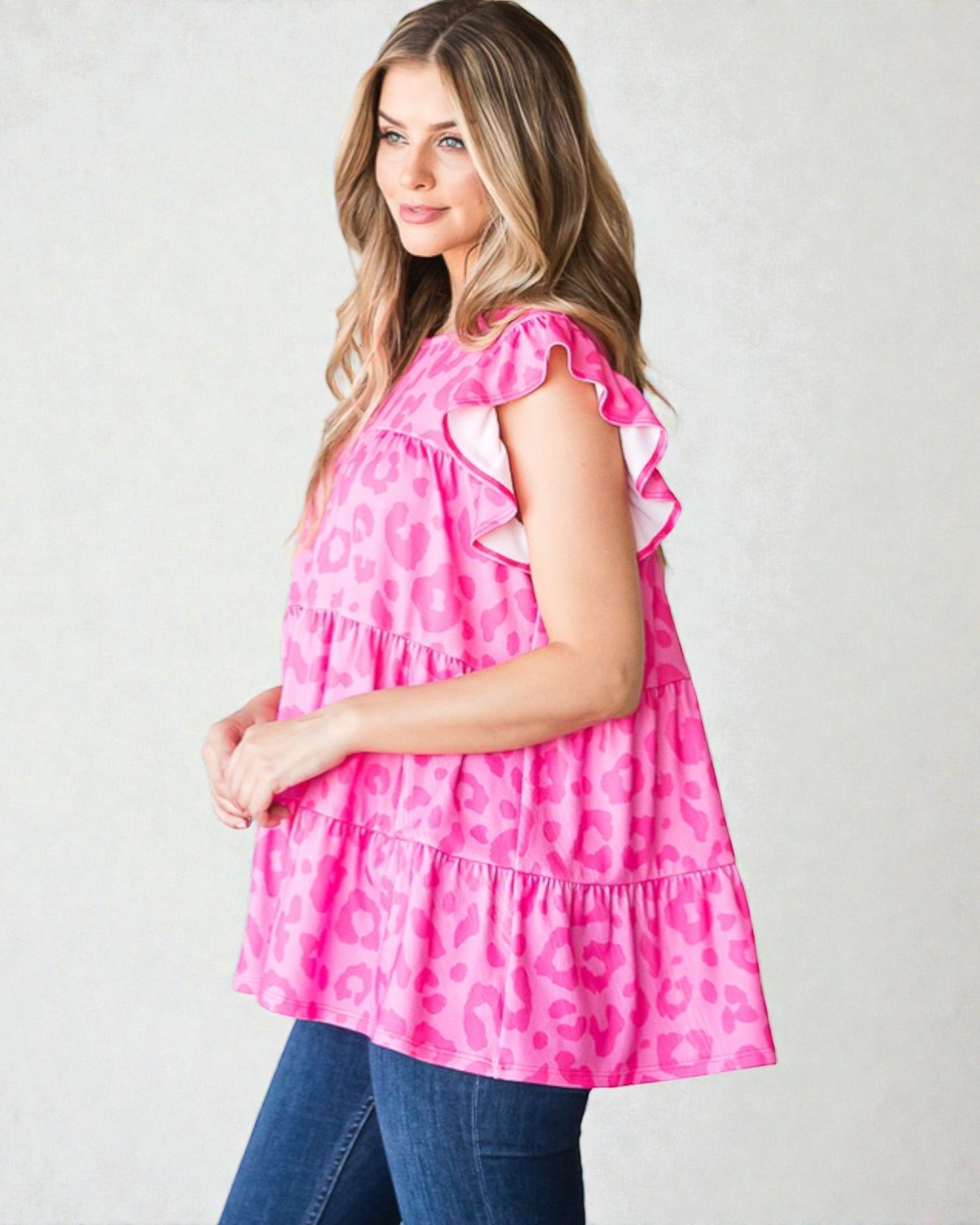 Woman wearing a pink patterned top with ruffled sleeves on a plain background