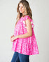 Woman wearing a pink patterned top with ruffled sleeves on a plain background