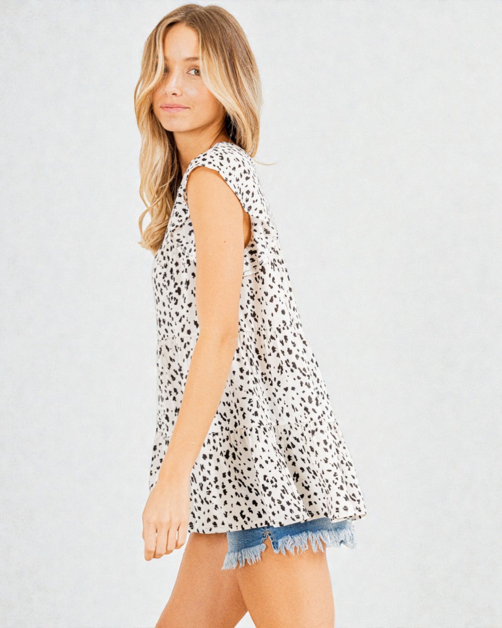Woman wearing a sleeveless animal print top and denim shorts on a plain background
